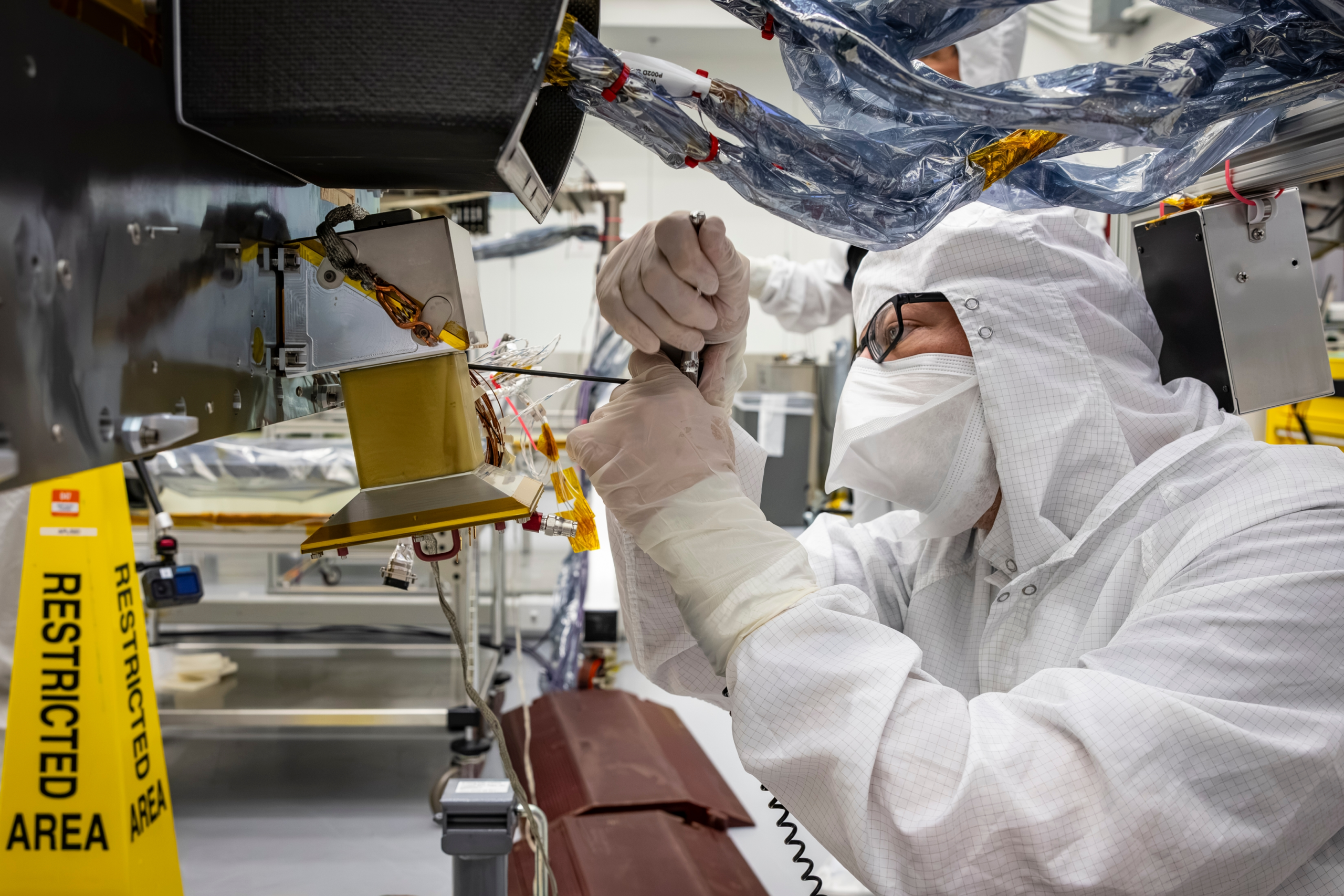 Technician Emory Toomey installs a navigation camera on NASA’s Dragonfly rotorcraft in a cleanroom