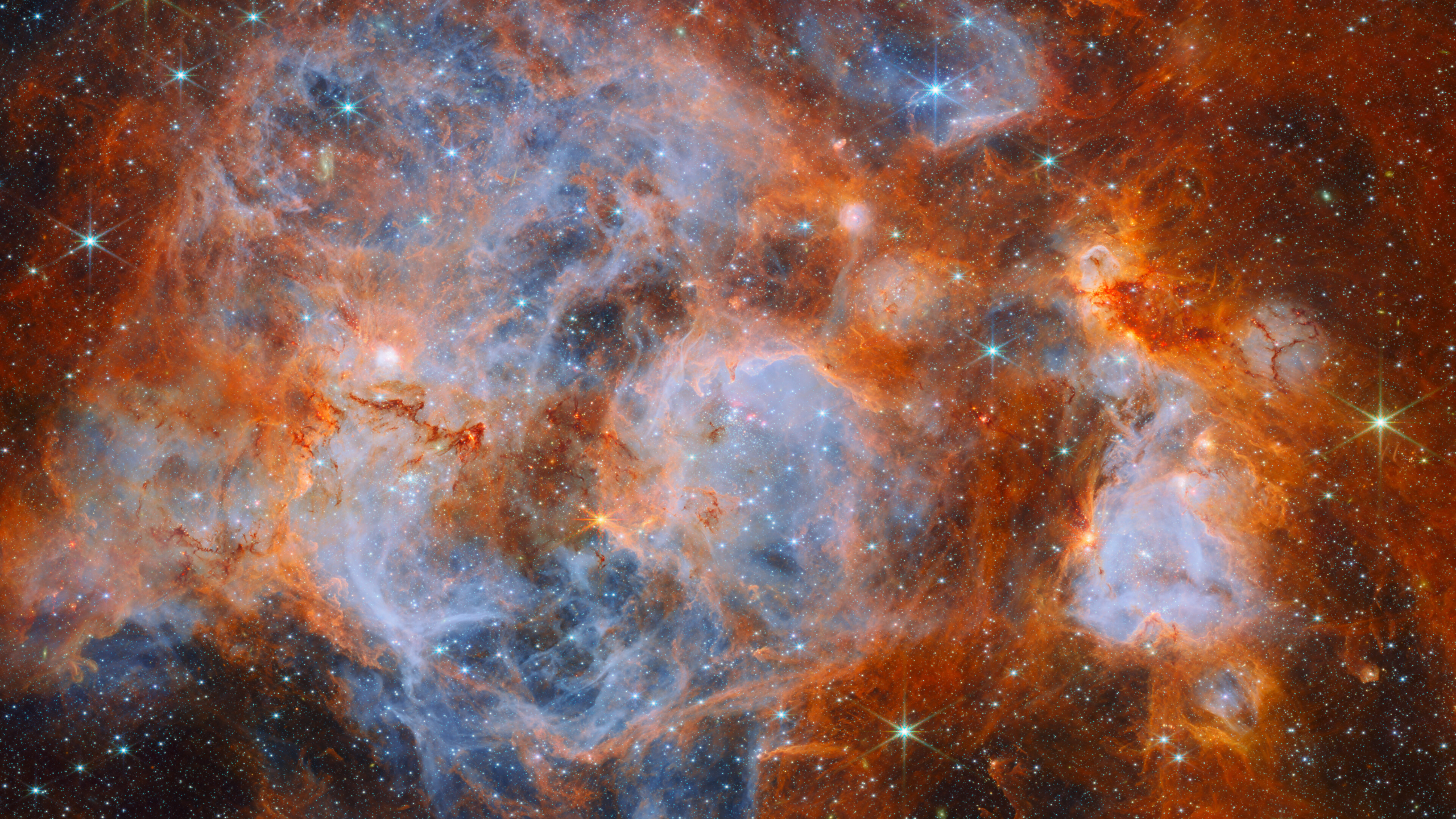 James Webb infrared panorama of N159 showing blue ionized bubbles, orange clouds, dark molecular filaments and thousands of stars