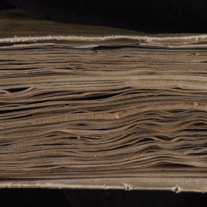 Head-on view of the Voynich Manuscript showing its layered parchment pages and binding