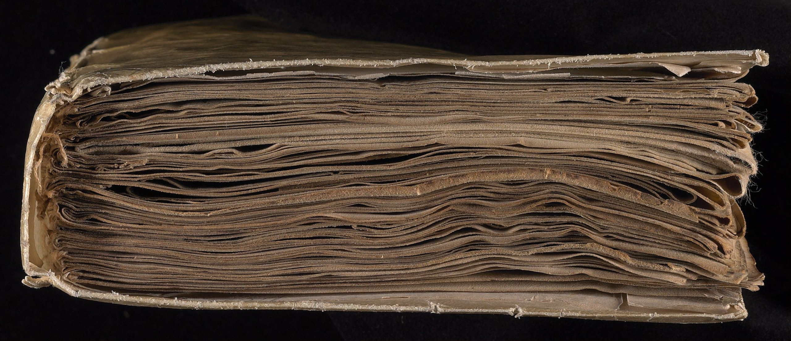 Head-on view of the Voynich Manuscript showing its layered parchment pages and binding