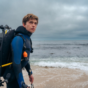 Austin Abrams as Jay Gardiner, wearing scuba gear on a beach in Whalefall.