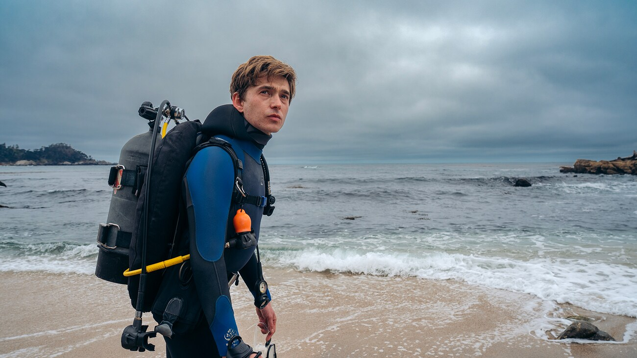 Austin Abrams as Jay Gardiner, wearing scuba gear on a beach in Whalefall.