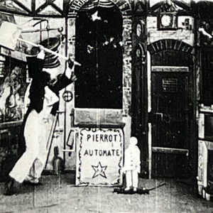 Black-and-white frame from the 1897 Georges Méliès film showing the Pierrot automaton beside its workshop sign; photographed from the recovered 35mm print.