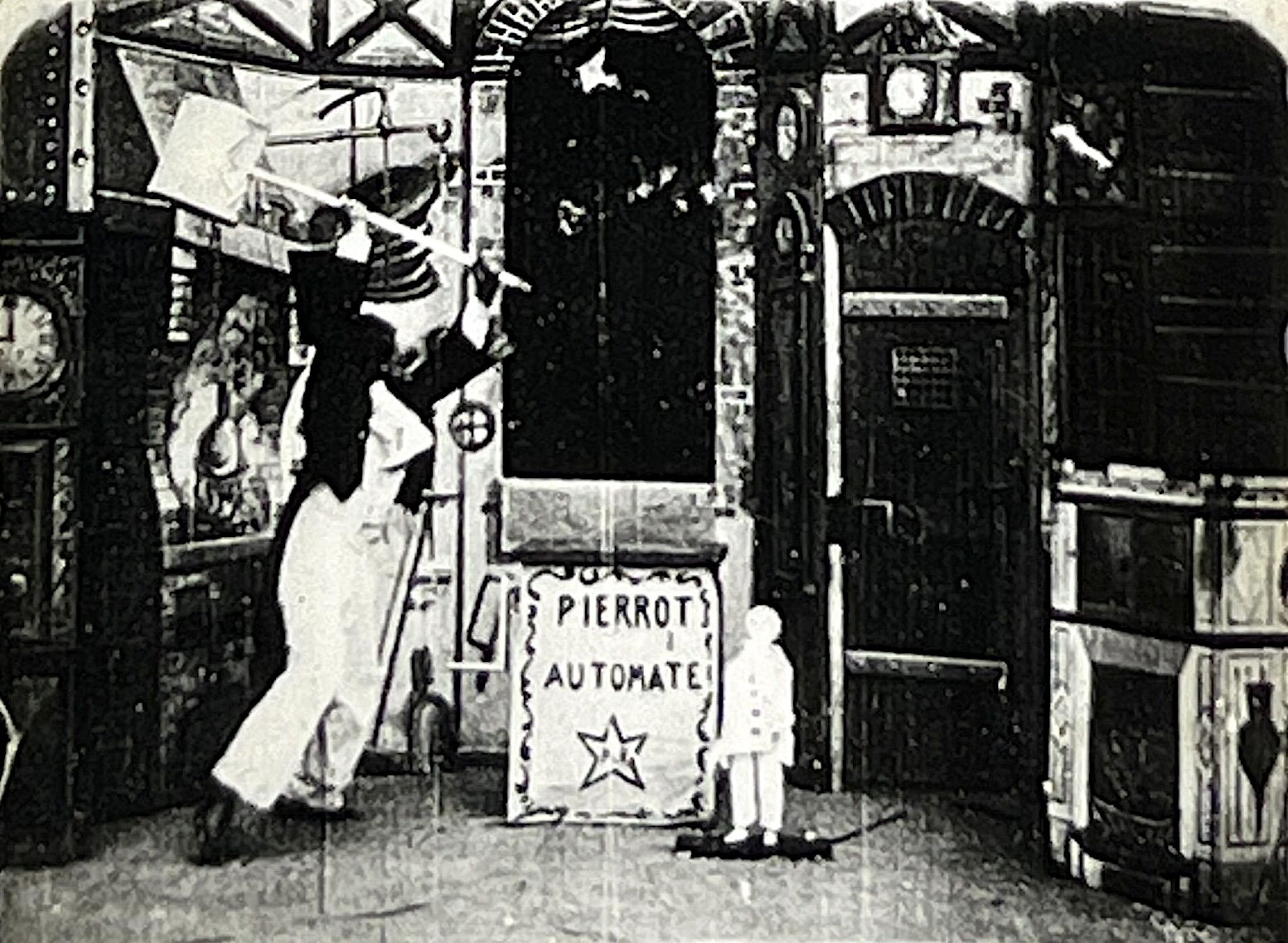 Black-and-white frame from the 1897 Georges Méliès film showing the Pierrot automaton beside its workshop sign; photographed from the recovered 35mm print.